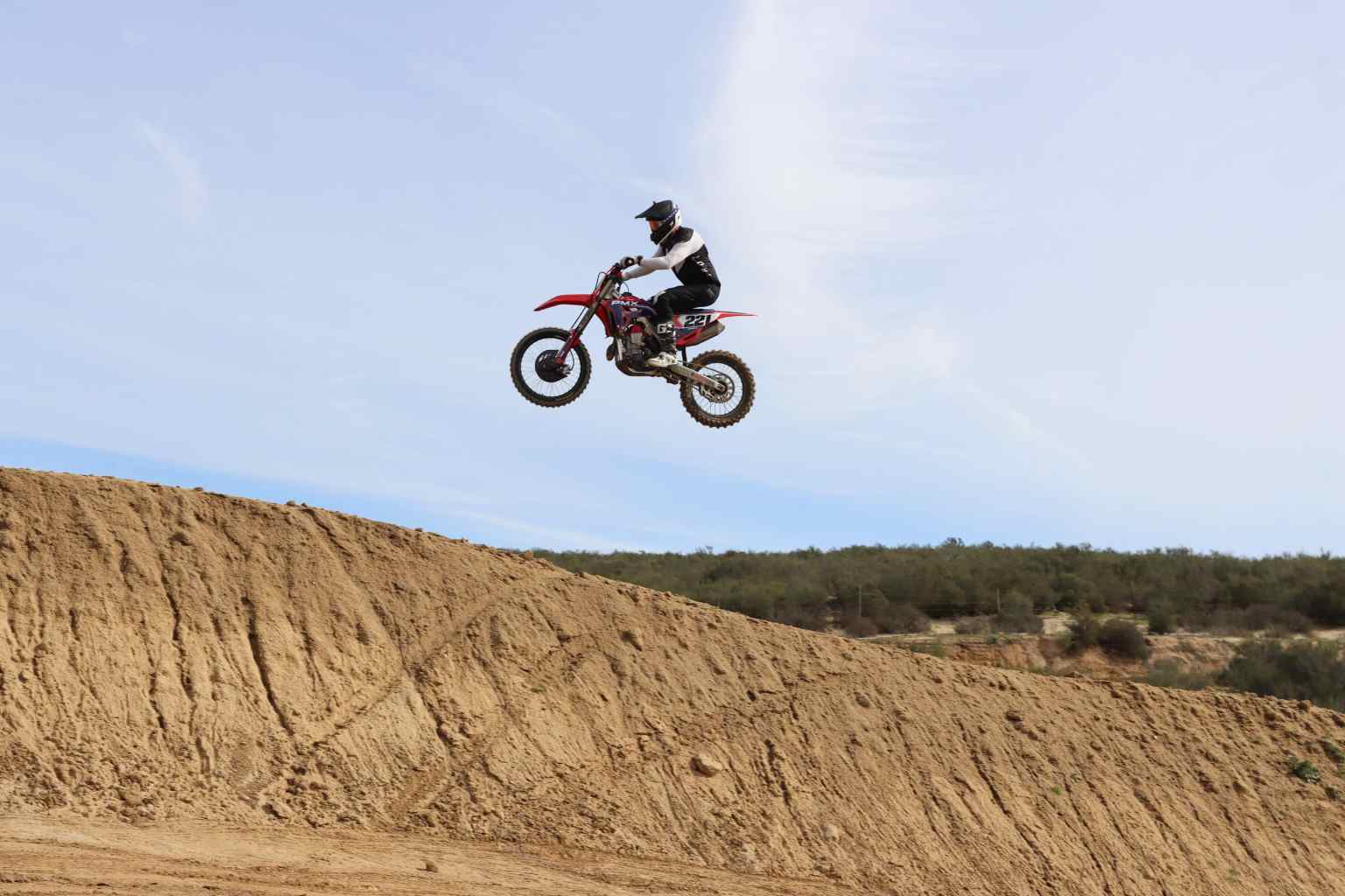 A motocross rider airborne over a dirt jump on a sunny day.