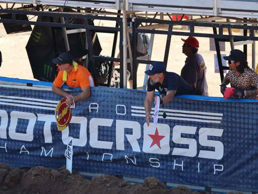 Spectators watching a motocross event at an outdoor track with a banner.