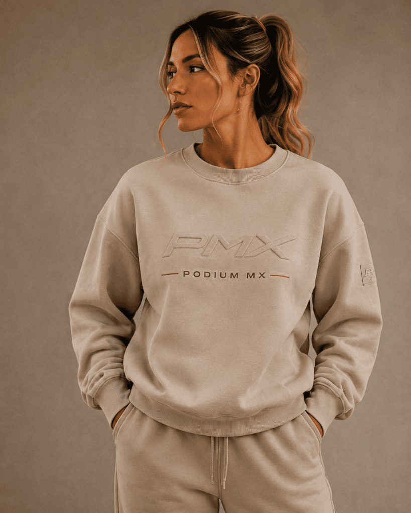 Woman in beige sweatshirt with "PMX Podium MX" logo, casual pose, neutral background.